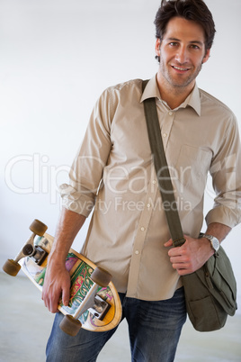 Casual businessman standing with his skateboard smiling at camer