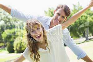 Attractive couple smiling at camera and spreading arms in the pa