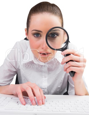 Businesswoman typing and looking through magnifying glass