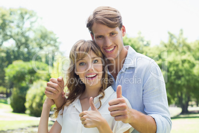 Attractive couple smiling at camera and showing thumbs up in the Attractive couple smiling at camera and showing thumbs up in the