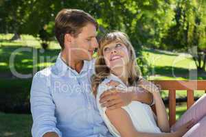 Affectionate couple relaxing on park bench together smiling at e
