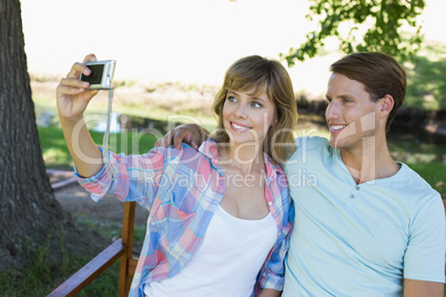 Cute couple sitting on bench in the park taking a selfie