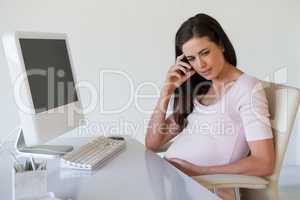 Casual pregnant businesswoman thinking at her desk