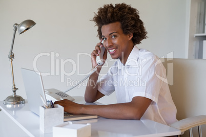 Focused casual businessman on the phone using laptop at desk