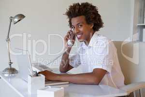 Focused casual businessman on the phone using laptop at desk