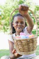 Little girl sitting on grass showing basket of easter eggs to ca