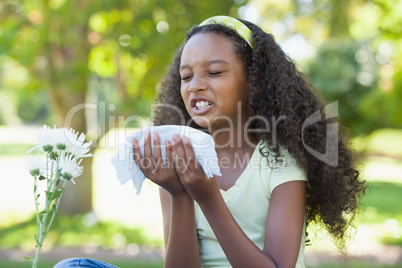 Young girl sitting by flower and sneezing in the park