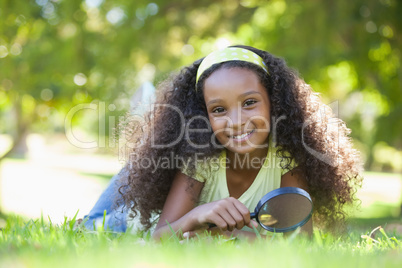 Young girl holding magnifying glass in the park smiling at camer