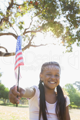 Little girl sitting on grass waving american flag