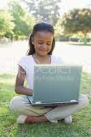 Little girl sitting on grass using laptop