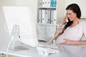 Casual pregnant businesswoman touching her bump at her desk talk