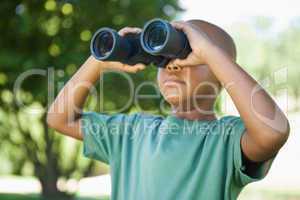 Little boy looking up through binoculars in the park