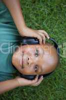 Little boy lying on grass listening to music smiling at camera