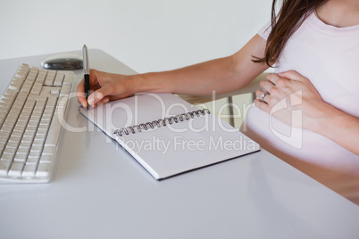 Casual pregnant businesswoman writing at her desk