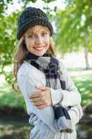Pretty blonde in hat and scarf smiling at camera in the park