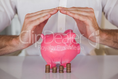 Casual businessman sheltering piggy bank and coins