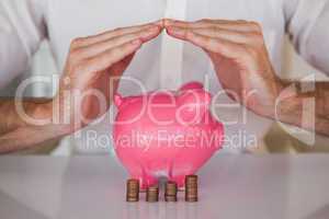 Casual businessman sheltering piggy bank and coins