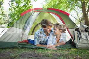 Cute couple lying in their tent smiling at each other