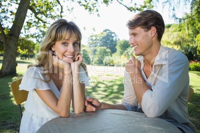 Cute couple sitting outside at a cafe with woman smiling at came