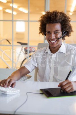 Casual young businessman using digitizer and headset at desk