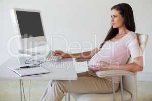 Casual pregnant businesswoman touching her bump at her desk