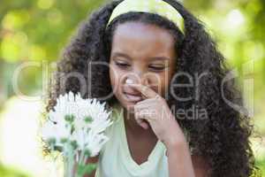 Young girl holding a flower and covering her nose in the park