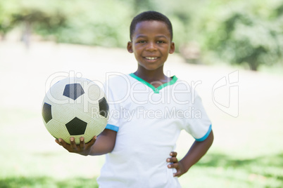 Little boy holding football in the park smiling at camera Little boy holding football in the park smiling at camera