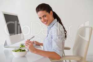 Casual brunette businesswoman eating a salad at her desk