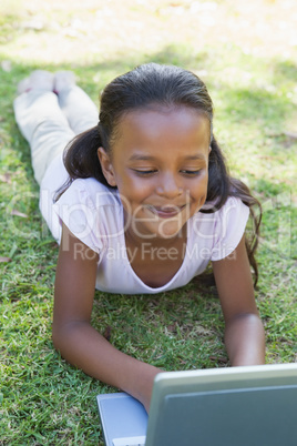 Little girl lying on grass using laptop