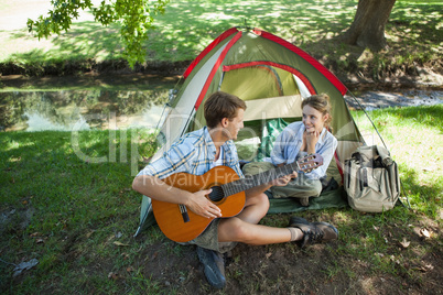 Cute man serenading his girlfriend on camping trip