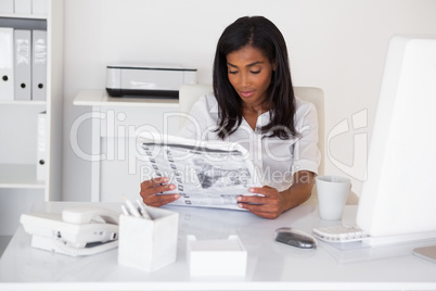 Pretty businesswoman reading newspaper at her desk