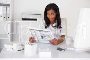 Pretty businesswoman reading newspaper at her desk