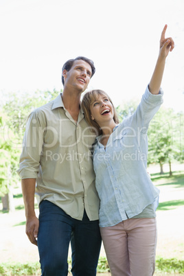 Carefree couple standing in the park with woman pointing