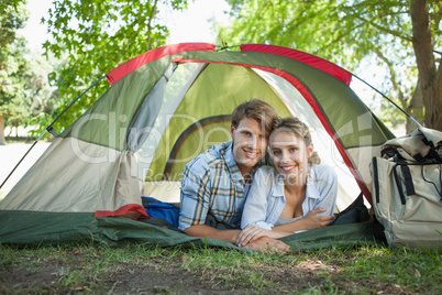 Cute couple lying in their tent smiling at camera