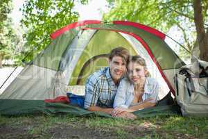 Cute couple lying in their tent smiling at camera