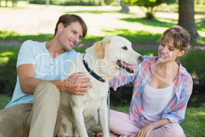 Happy couple sitting with their labrador in the park