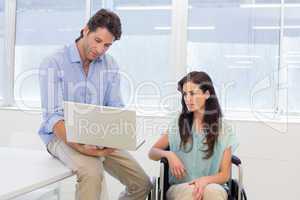 Businessman showing woman in wheelchair the laptop