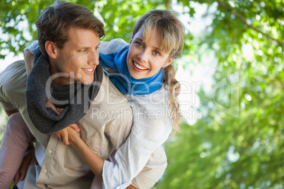 Cute woman smiling at camera in the park while getting a piggy b