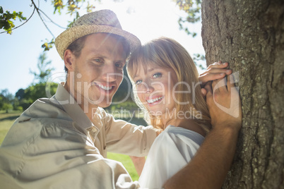 Cute couple leaning against tree in the park smiling at camera