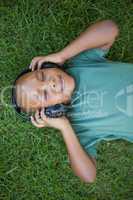 Little boy lying on grass listening to music with eyes closed