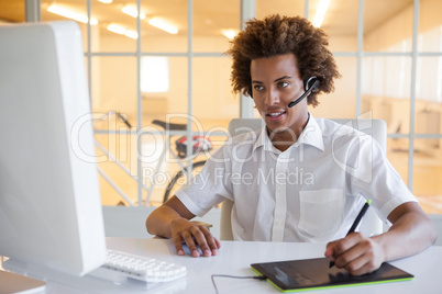 Casual young businessman using digitizer and headset at desk