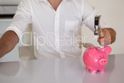 Casual businessman breaking piggy bank with hammer