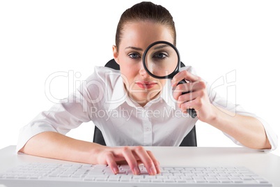 Businesswoman typing and looking through magnifying glass