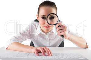Businesswoman typing and looking through magnifying glass