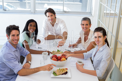 Business people smiling at camera eating sandwiches and fruit fo