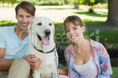 Happy couple sitting with their labrador in the park smiling at