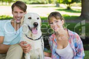 Happy couple sitting with their labrador in the park smiling at