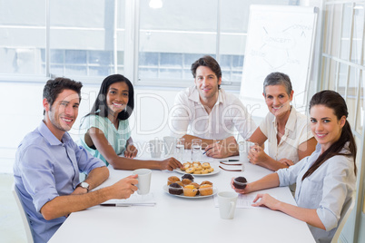 Work colleagues having hot beverages and muffins and smiling at