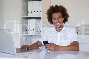 Casual smiling businessman using his smartphone and laptop at hi