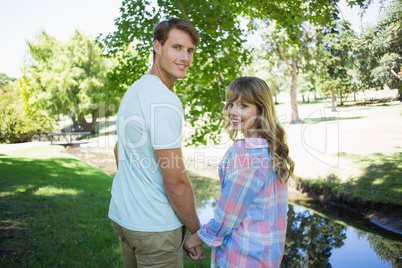 Cute couple walking hand in hand in the park smiling at camera